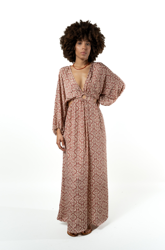 Three-quarter front view of a woman modeling a pink leaf print maxi dress with a plunging neckline and gathered waist.