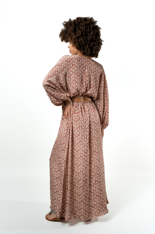 Back view of a woman in a pink patterned bohemian maxi dress showing the open back design with long loose sleeves.