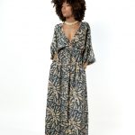 "Model wearing a long grey patterned maxi dress with deep V-neck, ring detail at the waist and balloon sleeves."