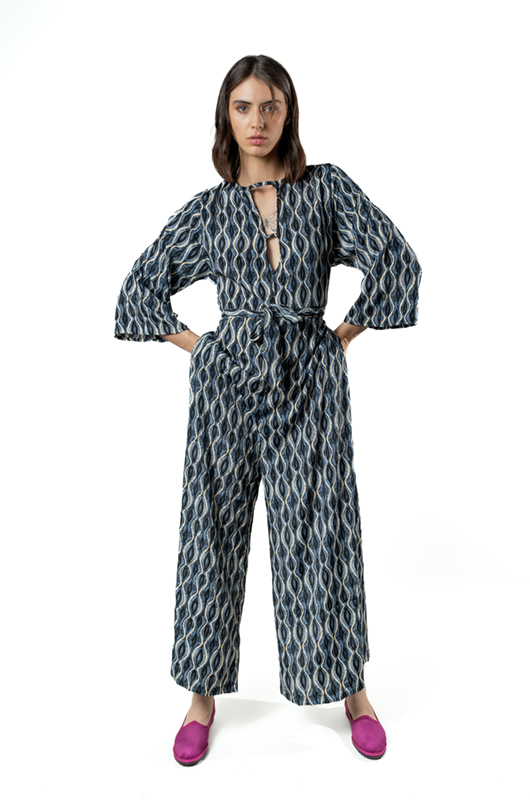 Studio shot of a model wearing a grey curves print jumpsuit with a keyhole neckline and wide-leg pants, paired with magenta flats.