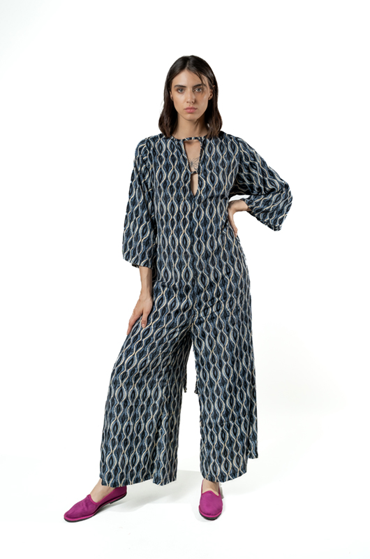 Studio shot of a model posing in a grey curves print jumpsuit with a tied waist and magenta flats.