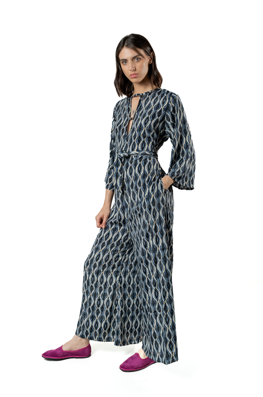 Side view of a model in a grey curves print jumpsuit with hands in pockets, wide-leg cut and magenta flats.
