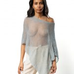Woman wearing a sheer blue poncho off one shoulder, paired with cream wide-leg pants.