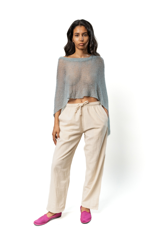 Front view of a sheer blue poncho with an asymmetrical hem, worn over cream wide-leg pants and bright pink slip-on shoes.