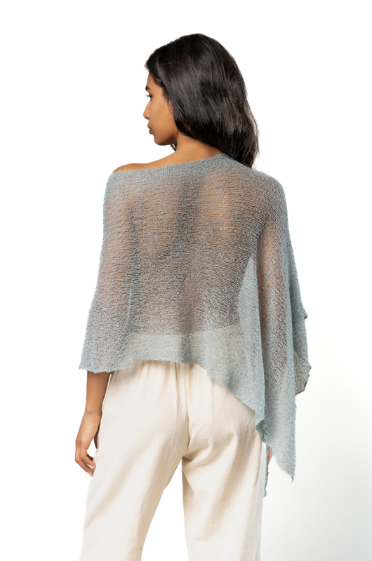 Back view of a sheer blue poncho with an asymmetrical hem, paired with cream wide-leg pants.