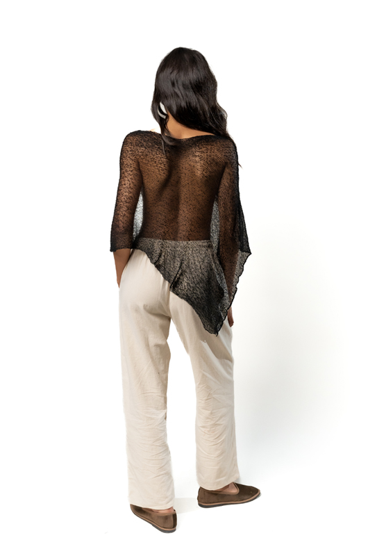 Back view of a sheer black poncho with an asymmetrical hem, worn over cream wide-leg pants.