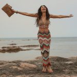 Model wearing multicolor crochet midi skirt in sunset tones by rocky shoreline, pair with a multicolor crochet crop top, front view