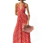 Woman wearing a black and beige patterned crop top and matching long skirt, holding a yellow beaded clutch bag, posing sideways.