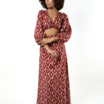 A model wearing a long red patterned co-ord set with a crop top and long skirt, posing with arms crossed.