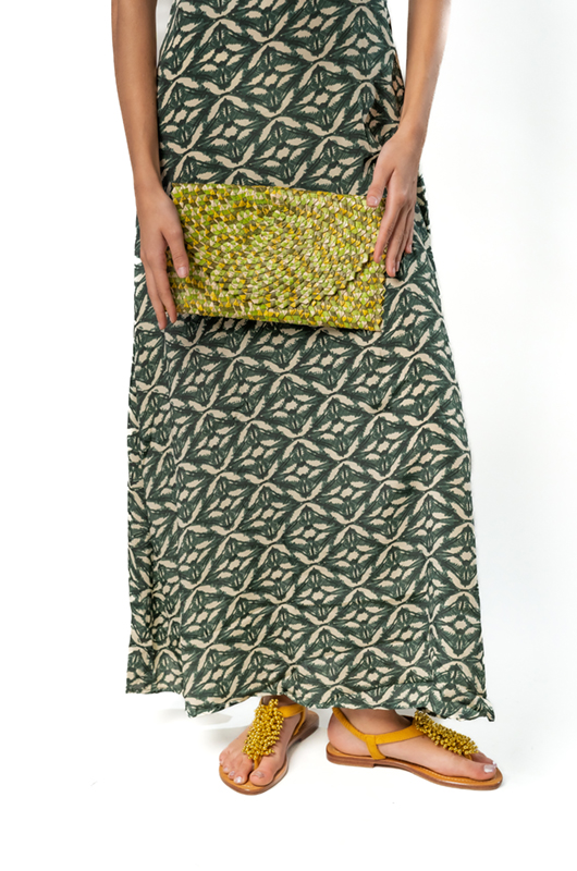 Woman in a black and beige patterned cropped top and matching maxi skirt, holding a small yellow beaded clutch in front, wearing green shoes.