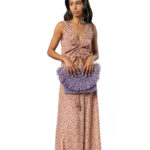 Woman in a green patterned halter maxi dress holding a violet fringed half-moon handbag above her shoulder.