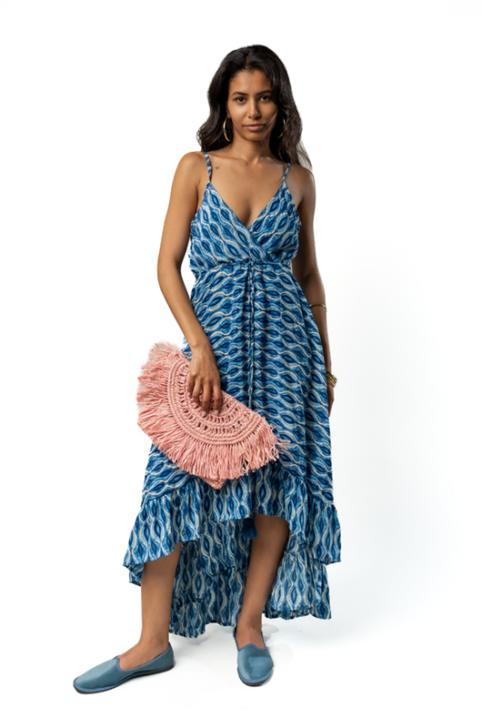 Woman in a blue patterned strappy dress holding a fuchsia woven clutch bag behind her back, with short curly hair