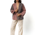 Model facing front wearing a quilted jacket in pink and dark blue micro-pattern, beige trousers, and brown shoes.